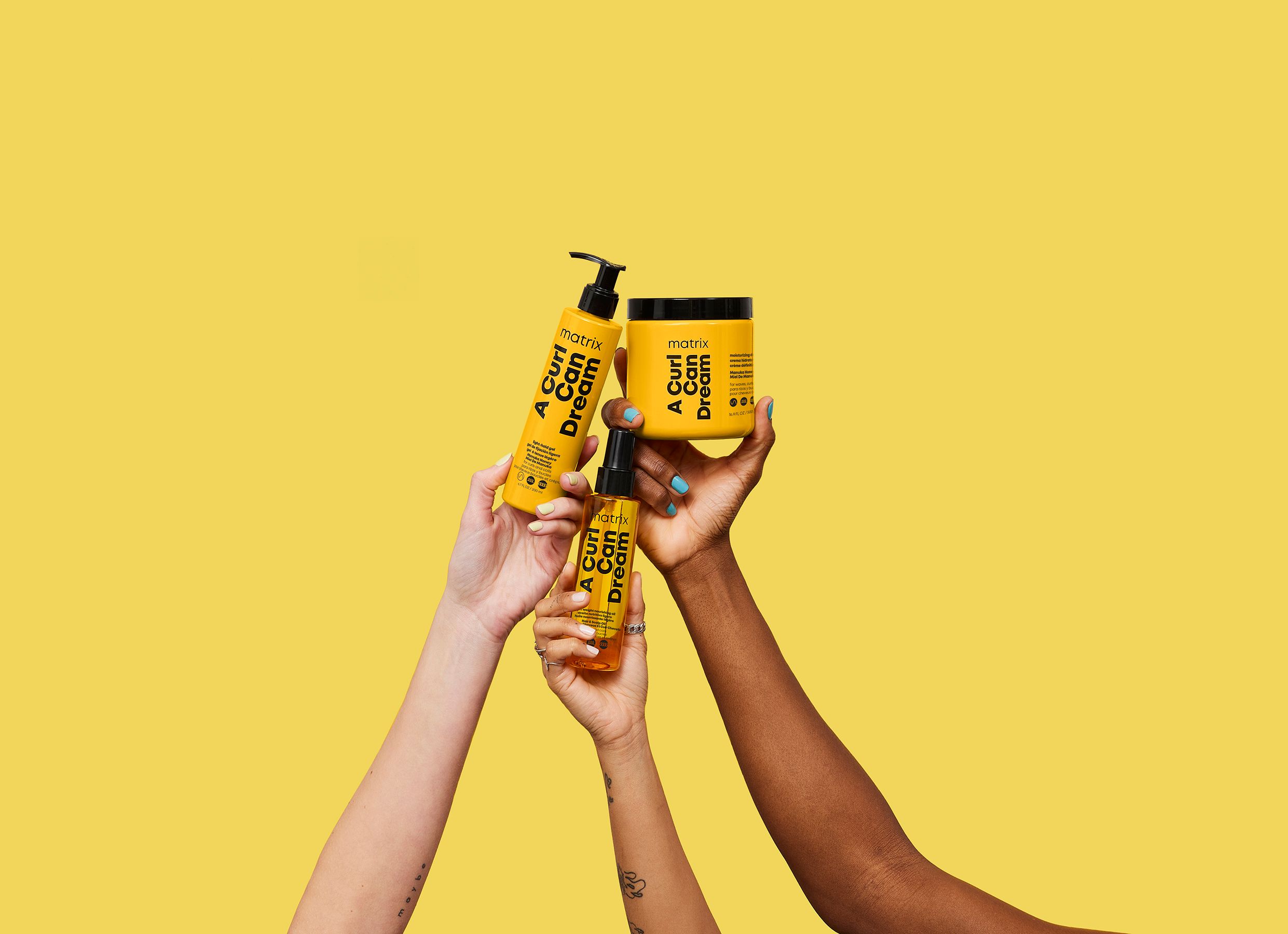 Matrix "A Curl Can Dream": three hands holding three SKUs against marigold. A bolder, more pop-forward voice for the Matrix audience.